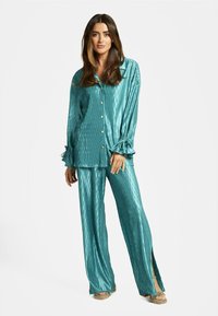 Conjunto de pijama de satén turquesa que incluye una camisa de botones con textura acanalada y puños atados, acompañada de pantalones de pierna ancha con aberturas laterales.