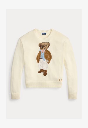 Kreemikas kampsun, millel on heegeldatud karu pruunis jopes ja prillidega, täiendatuna helehalli särgi ja valgete pükstega.