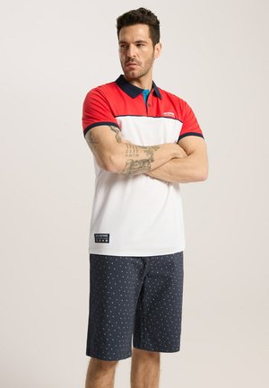Polówka z krótkim rękawem w kolorze czerwonym, białym i granatowym, z kołnierzykiem i logo, zestawiona z granatowymi szortami w mały biały wzór w kropki.