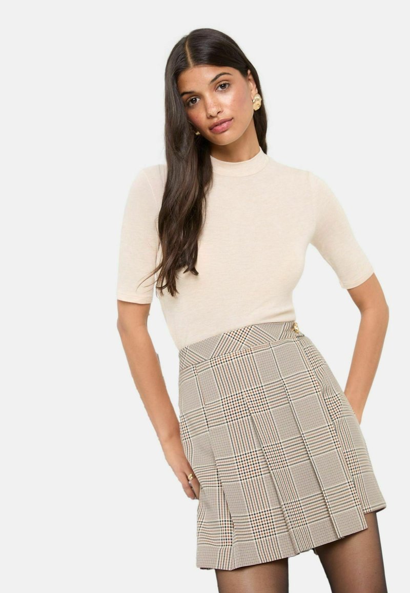Beige aansluitend topje met korte mouwen, gecombineerd met een geruite ploois rok in een mix van lichtbruin, crème en oranje patronen.