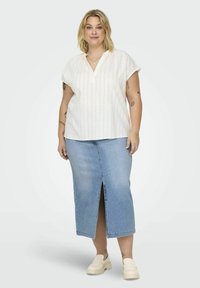 Blusa corta de manga corta a rayas blancas con cuello, combinada con una falda lápiz de mezclilla azul claro con una abertura frontal, llevada con zapatos de plataforma beige.