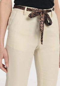 Beige Hosen mit glatter Textur, ausgestattet mit einem gemusterten braunen und schwarzen Knoten-Gürtel, entworfen mit Seitentaschen und einer taillierten Silhouette.