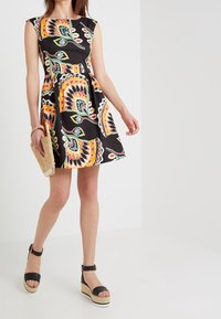 Mustapuku, jossa on värikäs paisley-kuvio, vyötärö korostuu ja hame on kellotettu. Yhdistetty mustiin platform-sandaaleihin ja punottuun käsilaukkuun.