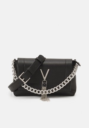 Sac bandoulière en cuir noir texturé avec une large bandoulière, un détail en chaîne argentée, et une fermeture en forme de V en argent avec des pampilles en chaîne pendantes.