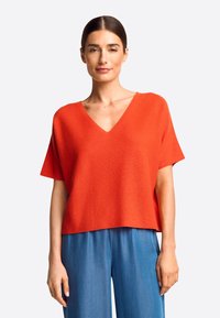 Rood, kortärmad pullover met een V-hals ontwerp, gemaakt van zachte gebreide stof. De zoom is iets verkort en heeft een ontspannen pasvorm.