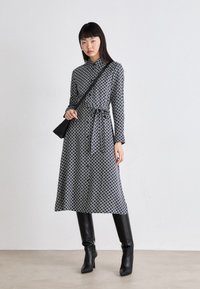 Abito a maniche lunghe con un motivo geometrico in bianco e nero, una cintura in vita e una lunghezza midi, abbinato a stivali neri al ginocchio.