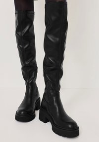 Czarne skórzane botki do kolan o eleganckim designie, teksturowanym wykończeniu i masywnej podeszwie z boku z zamkami błyskawicznymi dla łatwego zakupu.