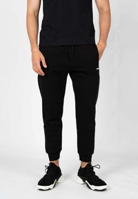Sorte sweatpants med en tætsiddende pasform, med elastiske manchetter og en justerbar snor i taljen. Kombineret med sorte sneakers.