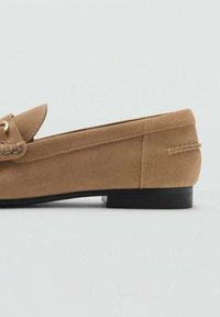 Bruna mockaläder loafers med svart sula och minimal sömnadsdetalj, visad från sidan på en enkel ljus bakgrund.