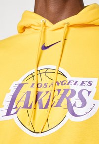 Sweatshirt amarelo com capuz e logo dos Los Angeles Lakers. Apresenta detalhes em roxo, bolso canguru e capuz com cordão. Feito de tecido macio.