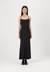 Črna, brezrokavna maksi obleka z oprijetim zgornjim delom, ravnim dekoltejem, tekočim krilom in subtilno raztegljivostjo. Nosi se z črnimi platform čevlji.