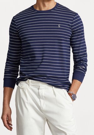 Marineblå langærmet skjorte med hvide vandrette striber, rund halsudskæring og broderet logo på brystet; kombineret med hvide bukser.