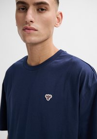 Mörkblå bomullströja med rund halsringning och korta ärmar, med en liten broderad logotyp på vänster sida av bröstet.