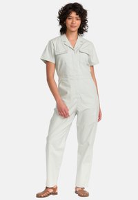 Lichtgroene jumpsuit met korte mouwen, twee borstzakken en een relaxte pasvorm. Inclusief een kraag en tapered pijpdesign.