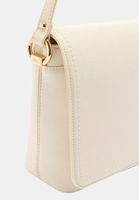 Beige lædertaske med et struktureret design, der har en guldfarvet metalaccent og syede detaljer langs kanterne.