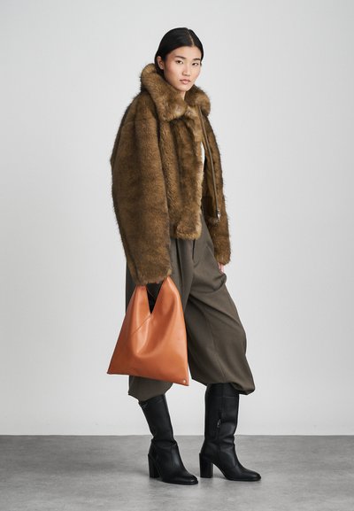 Brun fuskpälskort jacka, olivgröna byxor, svarta knähöga stövlar och en orange läderväska med en spetsig form. Släta texturer och rika färger.