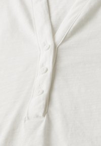 Maglietta henley bianca in cotone con tessuto a trama, caratterizzata da un colletto a V e cinque bottoni lungo la chiusura.