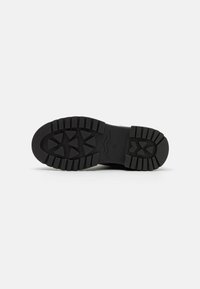 Semelle de botte en caoutchouc noir avec un motif de traction profond, comportant des crampons angulaires et une zone de bout lisse et arrondie. Construction texturée et robuste.