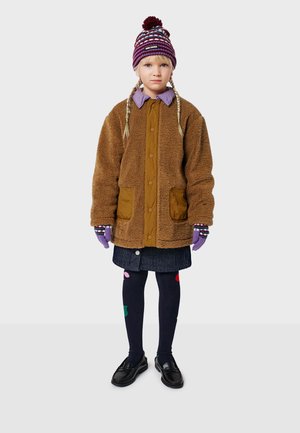Veste en polaire marron avec fermeture à boutons et poches avant, associée à une chemise à col violette, un chapeau rayé, des gants et des collants à motifs.