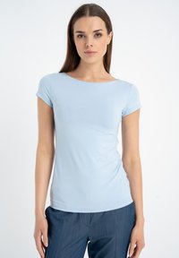 Jasnoniebieska koszulka z krótkim rękawem wykonana z elastycznego materiału, z okrągłym dekoltem i dopasowanym krojem, noszona z ciemnoniebieskimi spodniami.