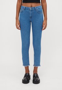 Jeans azuis ajustados com uma cintura de altura média, bainha desfiada e design clássico de cinco bolsos, combinados com sapatos pretos chunky de slip-on.