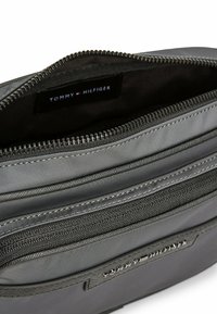 Bolsa de nailon gris con múltiples compartimentos con cremallera y un interior de tela. Presenta una etiqueta de marca visible en el interior, con costuras en contraste.