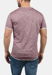 Bordeaux kortermet t-skjorte med teksturert finish og hvit kant rundt halsen og ermene, brukt med blå jeans.