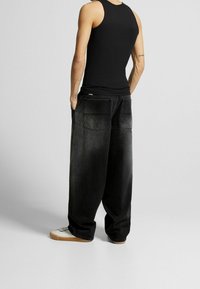 Svart linne, baggy svarta denimbyxor med texturerad yta, synliga sömmar och två stora bakfickor. Vita sneakers med gummisulor.