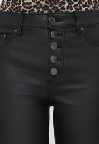 Hoge taille zwarte faux leren broek met knoopsluiting van vijf knopen, voorzakken en een stijlvolle textuur, met decoratieve stikseldetails.