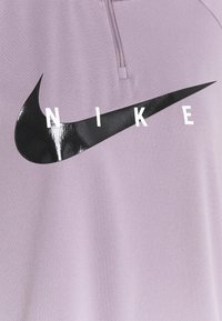 Violetti urheilupaita, jossa on neljänneksen mittainen vetoketjusuljin, suuri musta Nike-swoosh-logo ja valkoiset kirjainpalikat, jotka muodostavat sanan "NIKE." Kevyt kangaspinta.