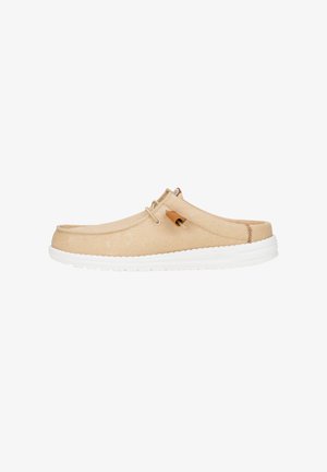 Zapato beis sin cordones con una parte superior de lona texturizada, suela de goma blanca y costuras mínimas. Presenta un pequeño acento marrón cerca del talón.