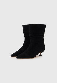 Stivali alla caviglia in suede nero con un design arricciato, punta affusolata e un distintivo tacco conico nero di piccole dimensioni. Texture liscia in tutto il corpo.
