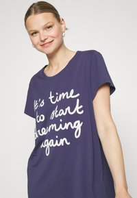 Fioletowa koszulka z krótkim rękawem, z białym, kursywnym napisem „Czas zacząć znowu marzyć”. Miękka bawełniana tkanina.