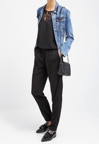 Veste en denim bleu clair, haut en dentelle noire, combinaison noire, mocassins noirs et un petit sac à bandoulière noir avec des clous et une chaîne de strap.