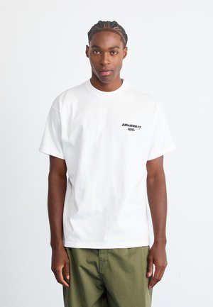 White cotton t-shirt with a round neckline and short sleeves, featuring black text logo on the left chest. Worn with green trousers.