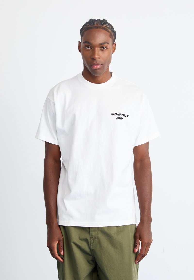 Witte katoenen T-shirt met een ronde halslijn en korte mouwen, met een zwart tekstlogo op de linkerborst. Draagbaar met groene broek.