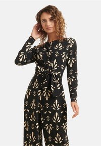 Long-sleeve black dress with a floral pattern in cream and red. Features a tied waist and a wrap design, made of smooth fabric.
