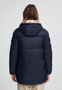 Granatowa kurtka puchowa z kapturem, z gładkim wykończeniem, poziomym pikowaniem oraz kontrastowym, różowym złotem wykończeniem przy kołnierzu.
