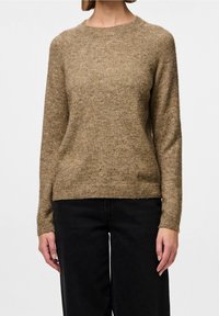Pull marron en tissu tricoté texturé, avec un col rond et des manches longues, associé à un pantalon noir.