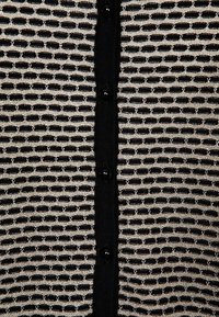 Schwarze und silberne Strickjacke mit einem strukturierten offenen Gewebe, Knopfverschluss und einfarbigem schwarzen Besatz entlang der Knopfleiste.