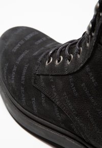 Černé semišové boty s texturovaným vzorem značky "Tommy Jeans", šesti kovovými očky a pevnou gumovou podrážkou.