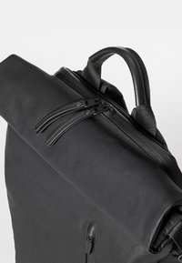 Schwarzer Rucksack mit einer strukturierten Oberfläche, doppeltem Reißverschluss und einem robusten Griff. Seitliche Reißverschlusstasche und gurtverstärkte Schulterriemen.