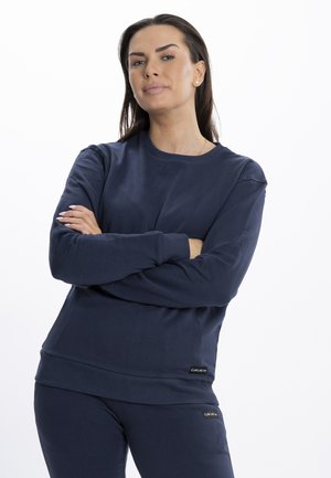 Sudadera de cuello redondo en color navy con mangas largas y puños acanalados. Presenta una textura suave y etiquetas de la marca en el dobladillo. Combinada con pantalones a juego.