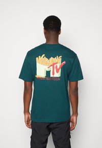 Zelené bavlněné tričko s grafikou hranolek v obalu a nápisem "MTV" v červené barvě, s nápisem "MUSIC TELEVISION" pod ním, krátké rukávy.