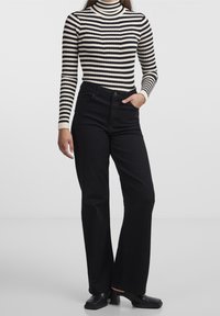 Czarne dzwony połączone z czarno-białym swetrem z golfem w paski. Bluzka ma teksturę prążkowaną i długie rękawy.