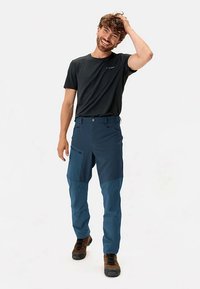 Lauko kelnės tamsiai mėlynos spalvos audinyje, su lygiu paviršiumi, su užtrauktuku užsegama kišene ir kontrastingais šviesesnės mėlynos spalvos akcentais. Dėvimos su juoda marškinėliais.