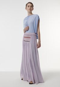 Lichtblauw top met een gedrapeerd ontwerp. Vloeiende lavendelkleurige rok met geraffineerde stof en decoratieve stiksels over de tailleband. Zwarte sandalen.