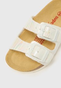 Bele sandale z dvema nastavljivima zaponkama, iridescentnimi trakovi in teksturirano ploskvijo iz plute. Imajo gladek gumijast podplat.