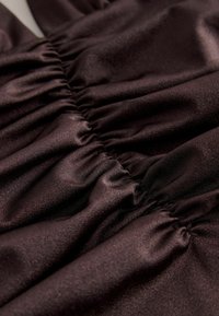 Primer plano de tela de satén marrón oscuro con textura fruncida y recogida que crea pliegues horizontales y un brillo sutil.