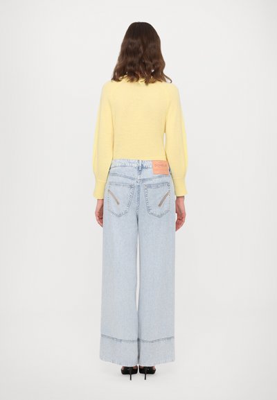 Kollane kudumissweater puhvade varrukatega, millele on sobitatud helesinised laiad püksid, millel on roosa brändi sild ja kontrastsed õmblusdetailid.
